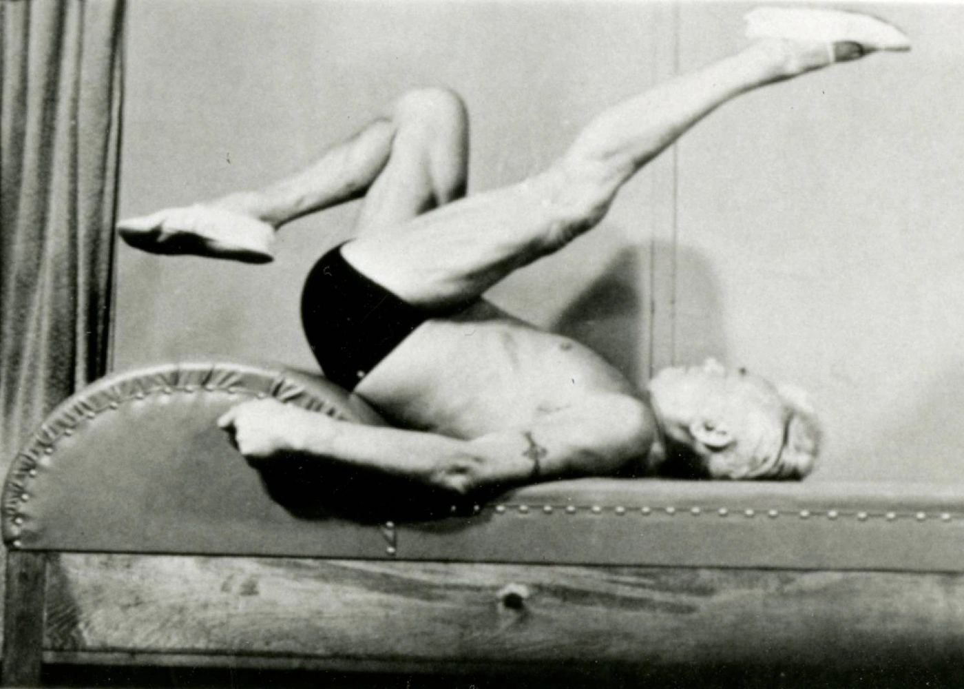 Photograph of Joseph Pilates laying on his back and stretching his leg up over his torso